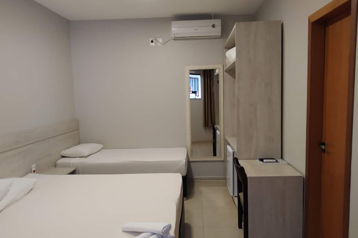 Habitación de hotel con dos camas individuales, un escritorio pequeño, un espejo y un armario.