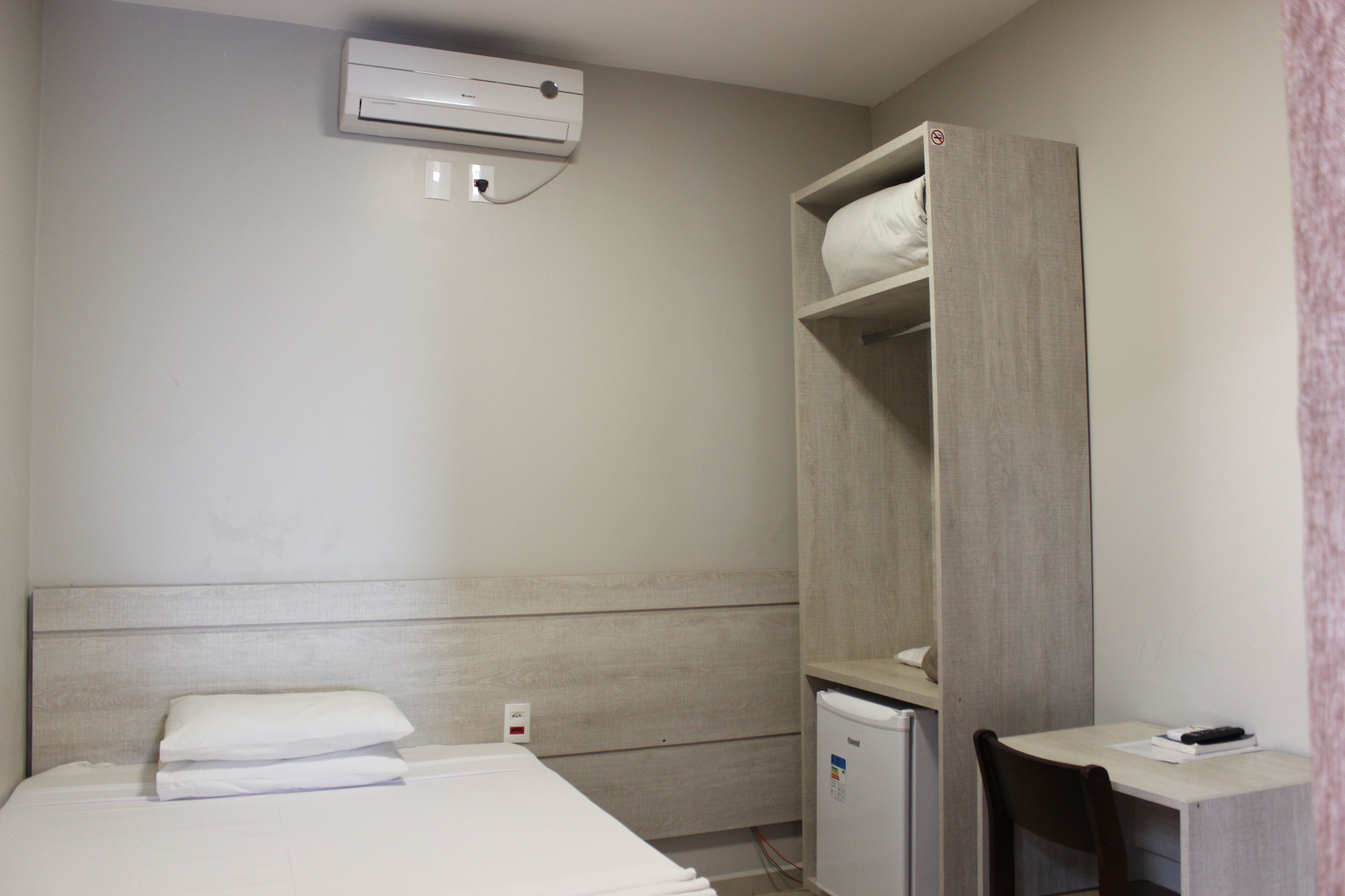 Une chambre d’hôtel équipée d’un lit, d’un bureau, d’une armoire et d’un petit réfrigérateur.