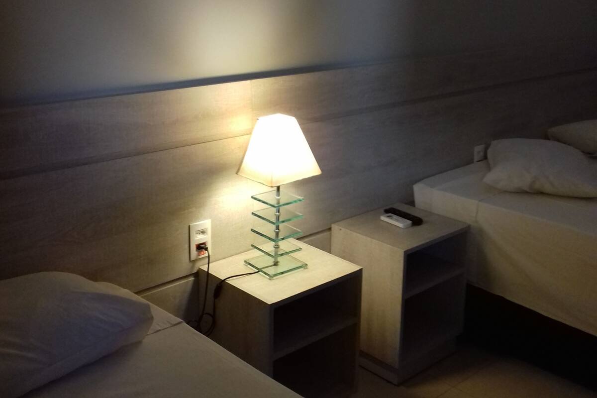 Una habitación de hotel con mesita de noche, lámpara, cama y mesita auxiliar.