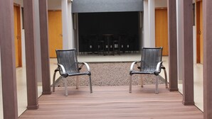 Een overdekt terras met twee stoelen en een tafel, dat uitkomt op een donkere ruimte.