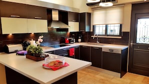 A modern kitchen with dark cabinetry, a central island, and a window with a view. - Villa Carlos (Patras)