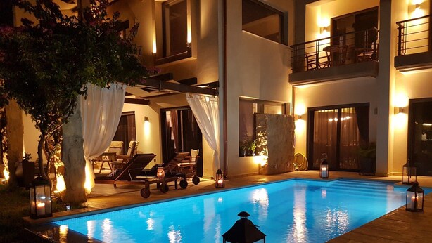 Una piscina con sillones de descanso y una pérgola, rodeada de un patio bien iluminado con vistas a un edificio de varios pisos.