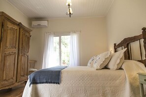 A bedroom with a bed, a wooden wardrobe, a window with curtains, and an air conditioning unit.