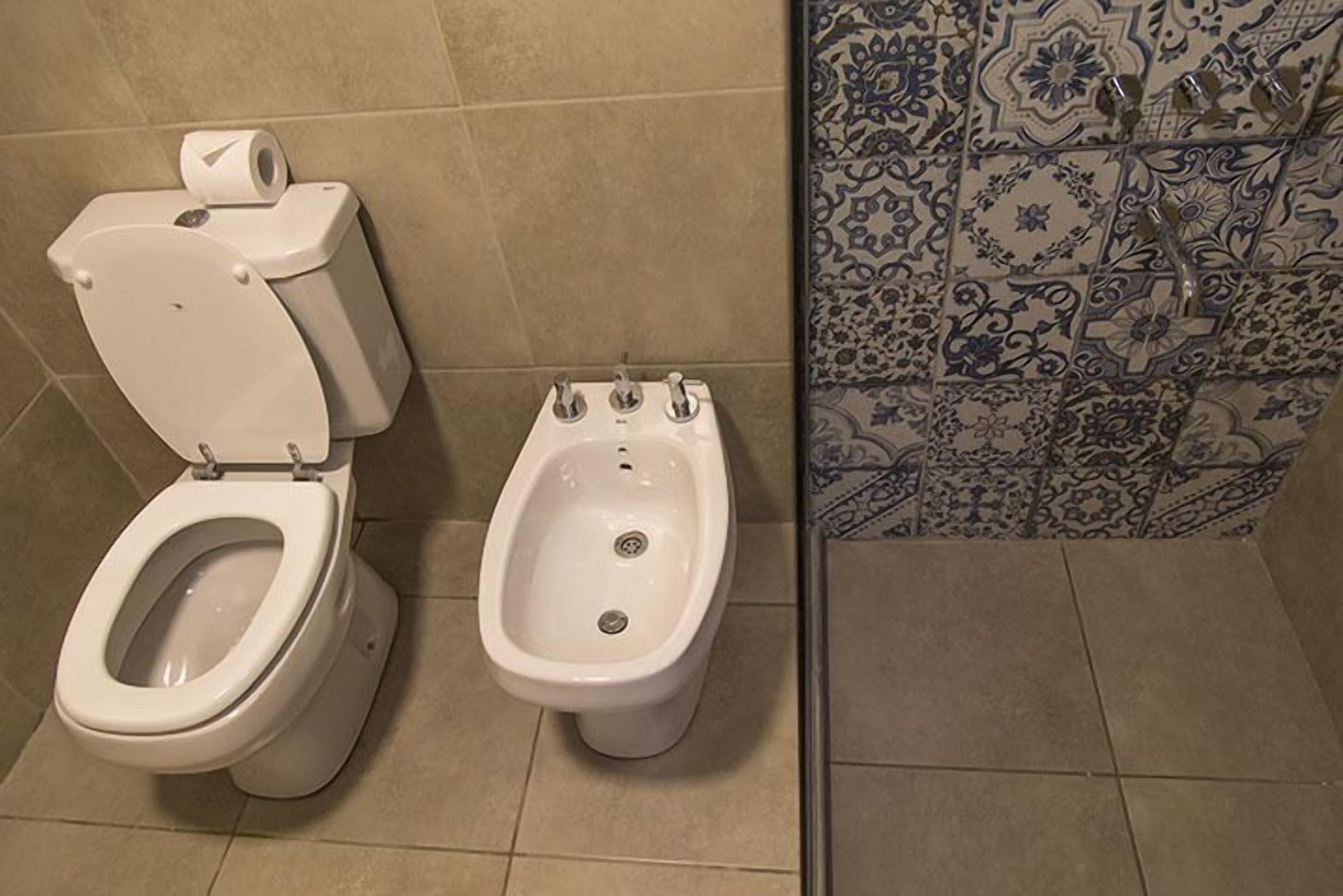 A bathroom with a toilet, bidet, and tiled walls.