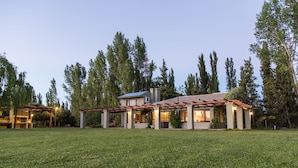 Une maison moderne dotée d’un patio couvert, entourée d’une pelouse bien entretenue et de grands arbres.