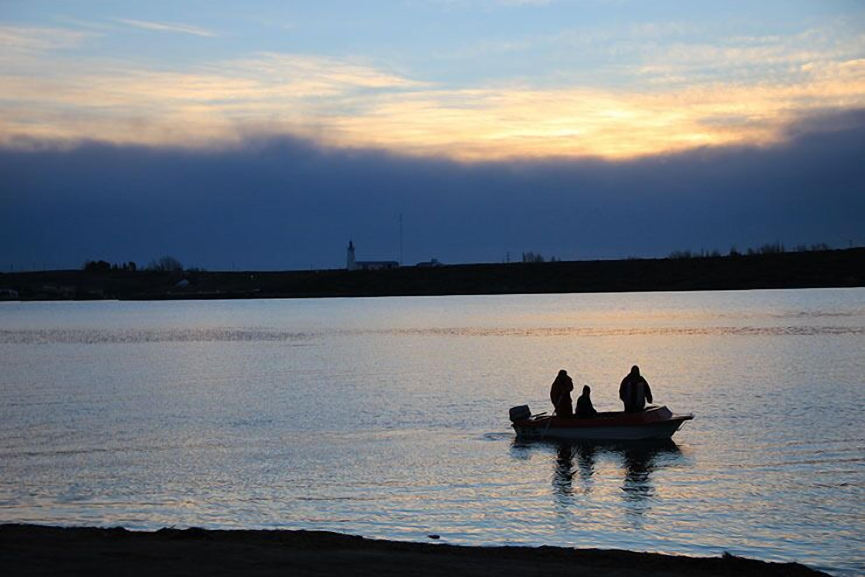 Una embarcación con dos personas en aguas tranquilas durante el atardecer.