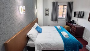 Una habitación de hotel con cama, escritorio, televisor y ventana con cortinas.