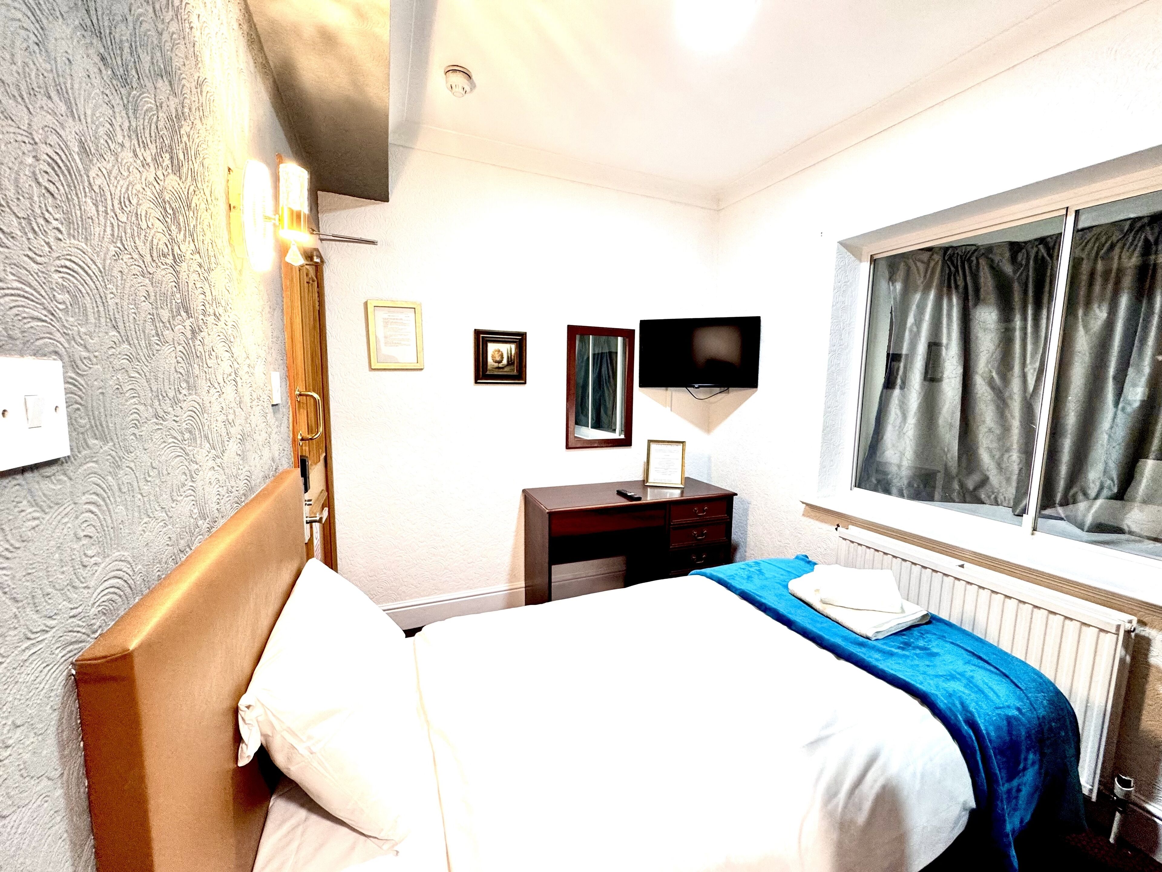 A hotel room with a bed, a dresser, a television, and a window with curtains.