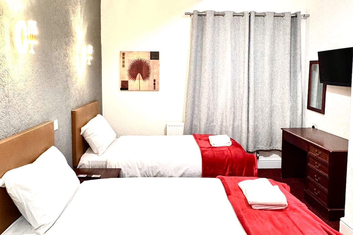 Quarto de hotel com duas camas, uma escrivaninha, penteadeira, televisão de tela plana e uma obra de arte na parede.