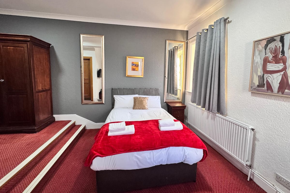 Quarto de hotel com cama, guarda-roupa de madeira, espelho, quadro e radiador.