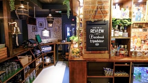 A bar area with a chalkboard sign, shelves with bottles, and hanging plants.