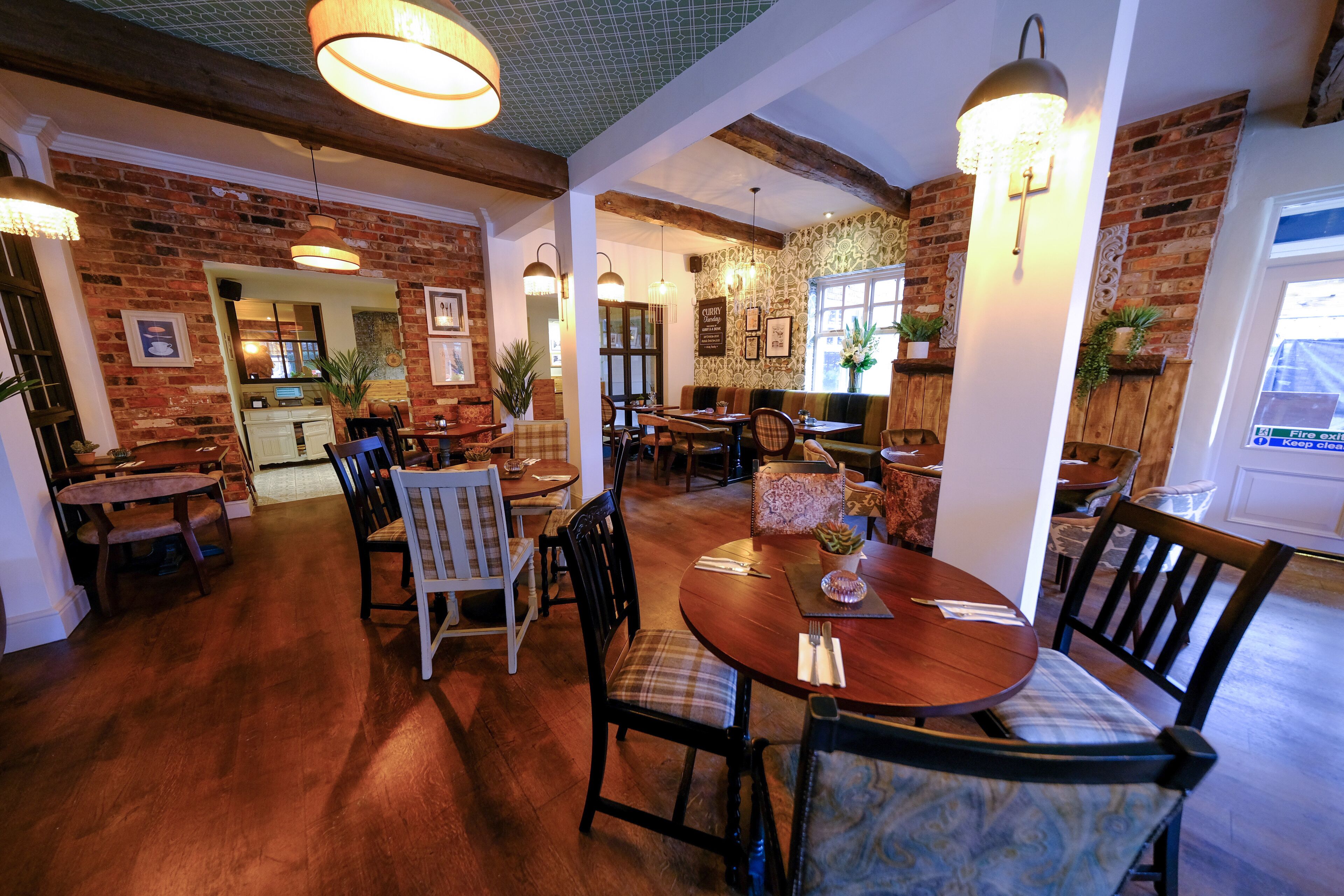 A restaurant with brick walls, wooden tables, and chairs. There are hanging lights and potted plants.