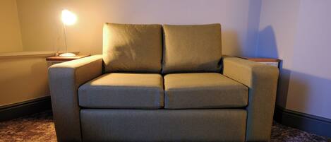 A single sofa in a room with a patterned carpet and a lamp on a side table.
