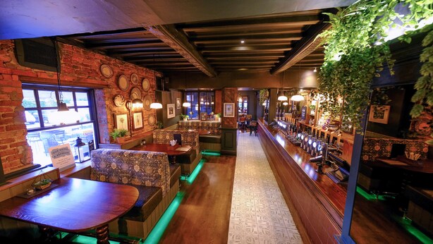 A cozy restaurant with brick walls, wooden tables, and green ambient lighting.