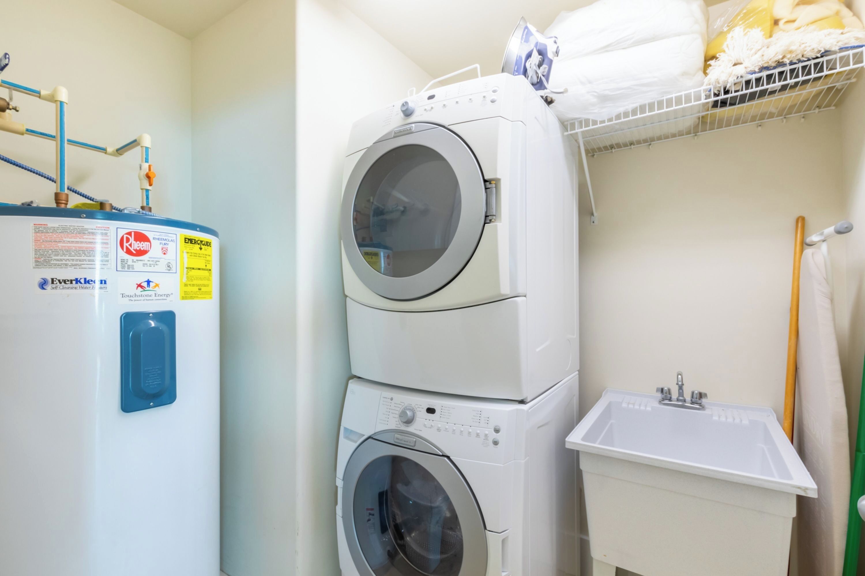 A laundry area with stacked washers and dryers, a sink, and a water heater.