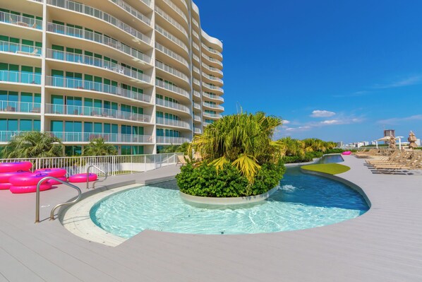 Uma área de piscina com piscina, espreguiçadeiras e um edifício com varandas.