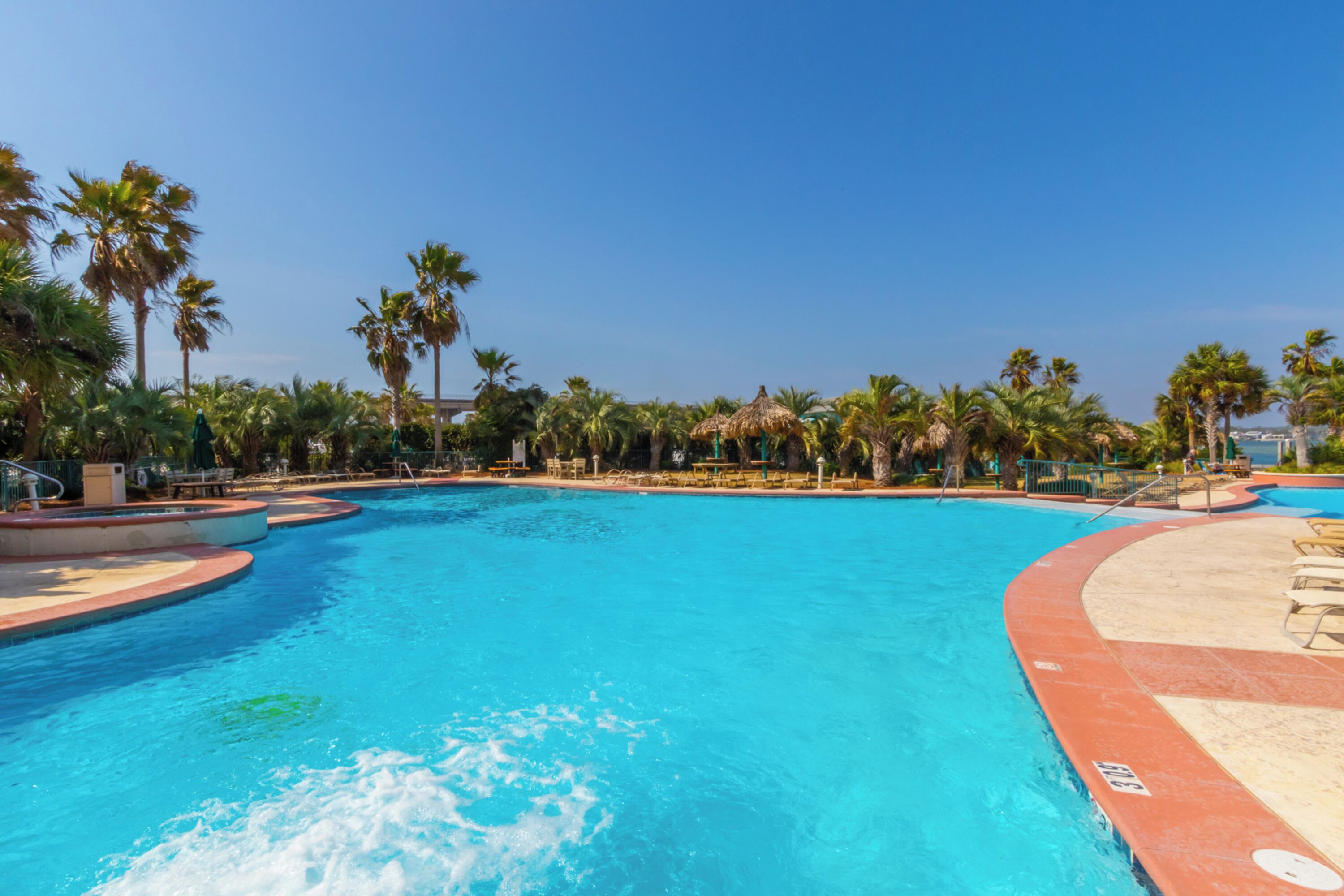 Una piscina amplia y cristalina rodeada de palmeras y sillones de descanso.