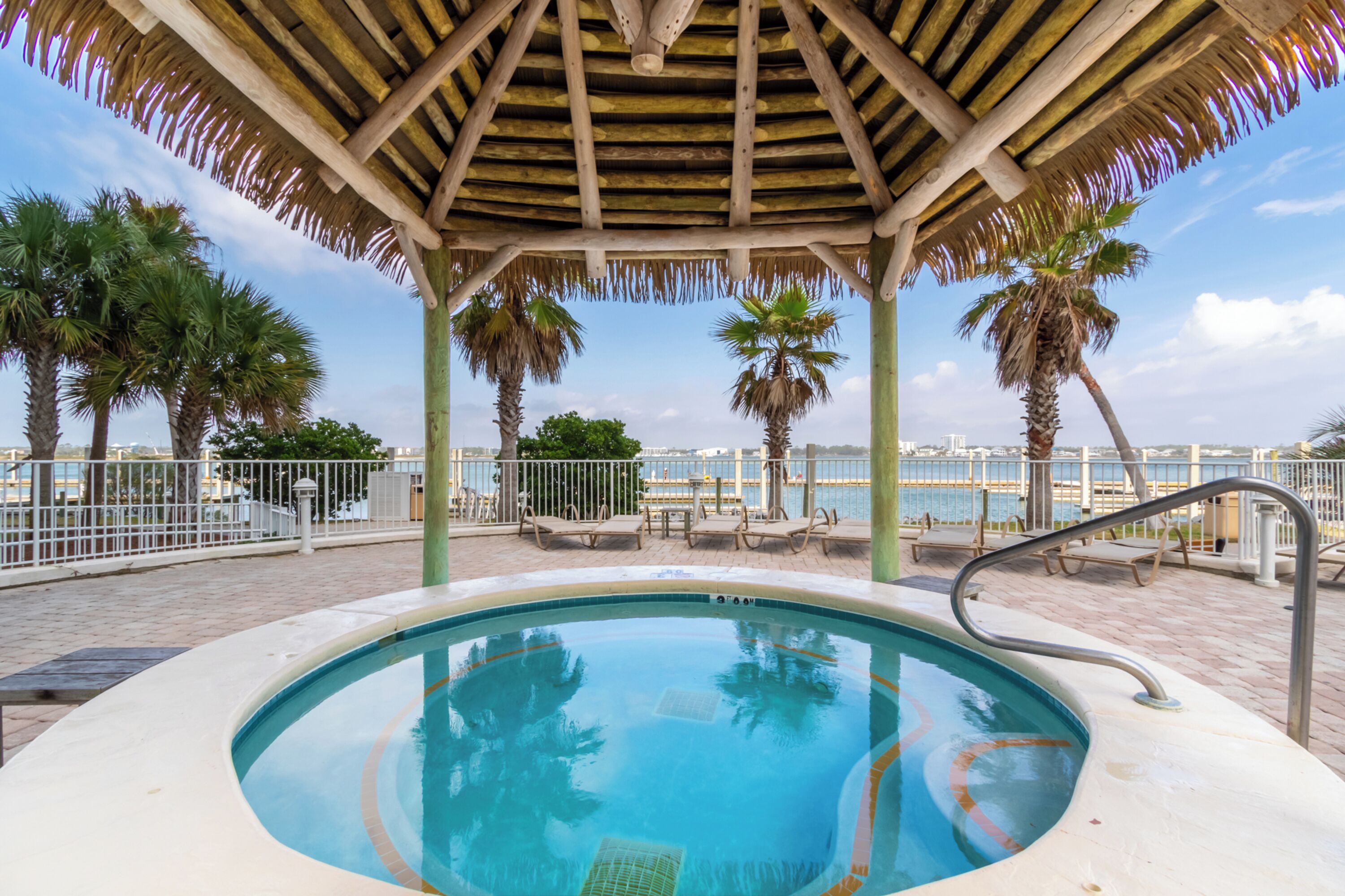 A pool area with a wooden pergola, palm trees, and a view of the water.