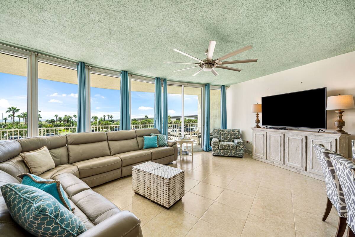 A spacious living room with a large sectional sofa, a television, and a ceiling fan.