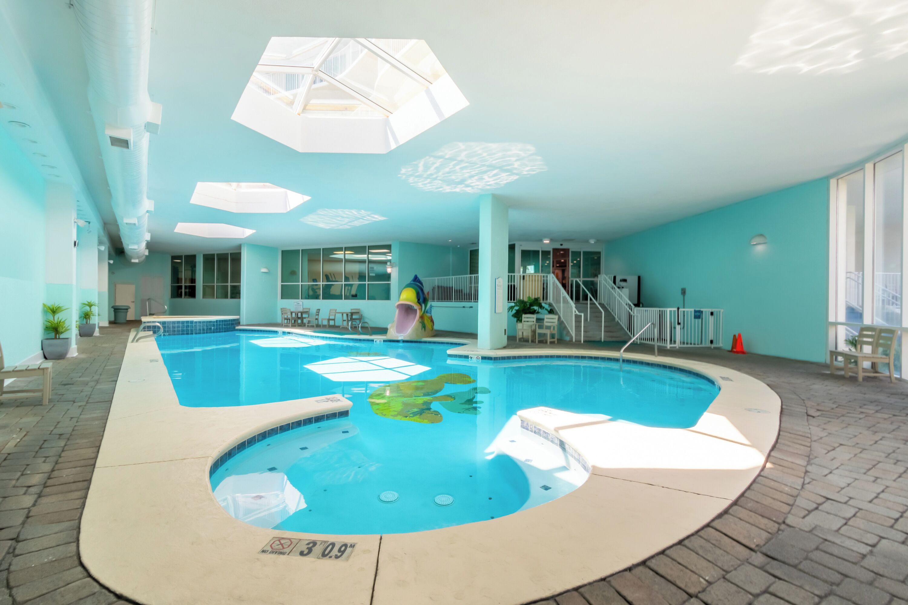 Una piscina interior con tobogán, zona de estar y vistas al cielo a través de amplios ventanales.