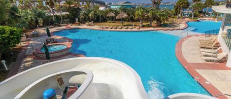 A large pool with a water slide, lounge chairs, and palm trees.