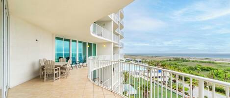 A balcony with a curved railing, outdoor seating, and a view of the ocean.
