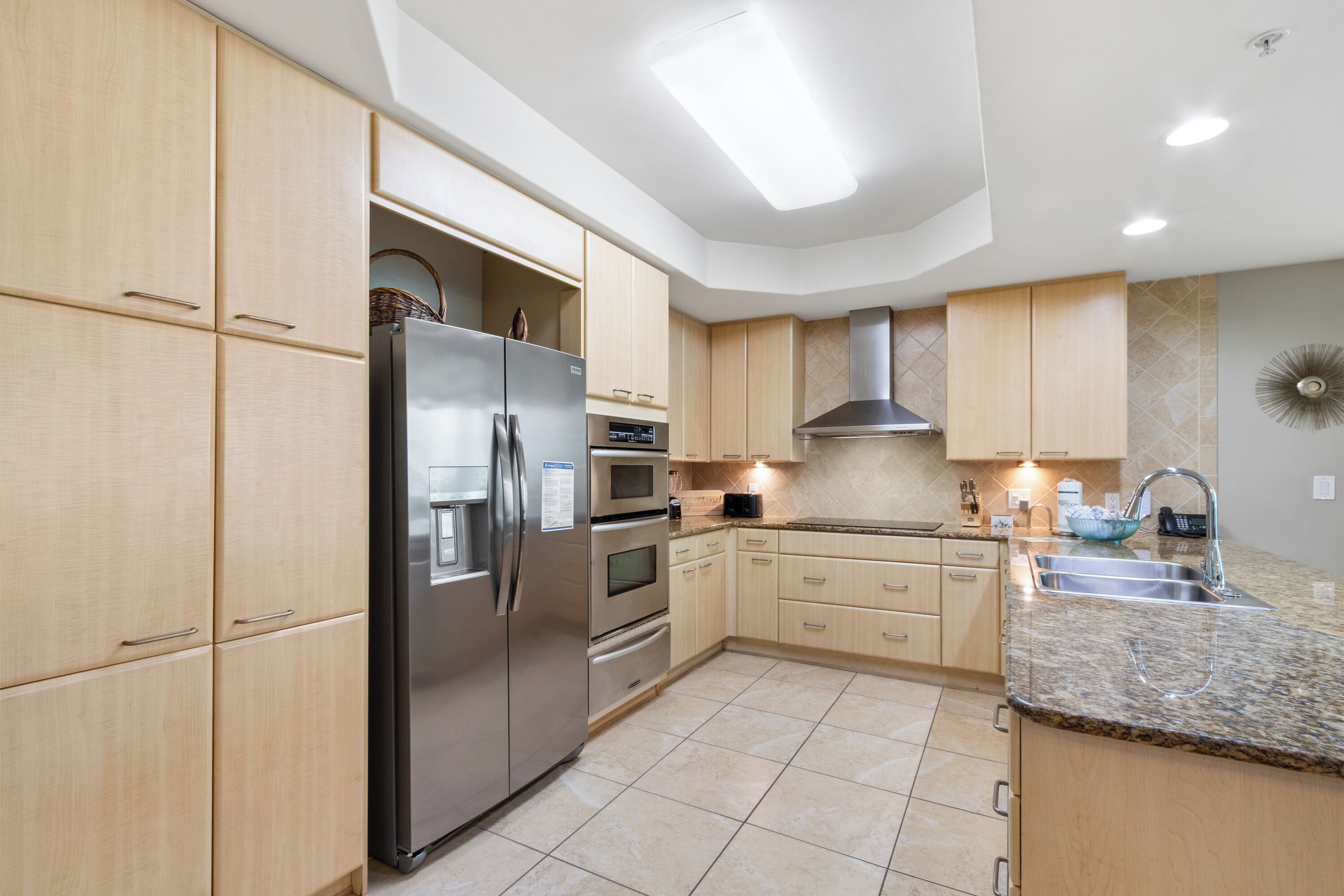 Una cocina moderna con armarios de madera clara, electrodomésticos de acero inoxidable, encimera de granito y horno integrado.