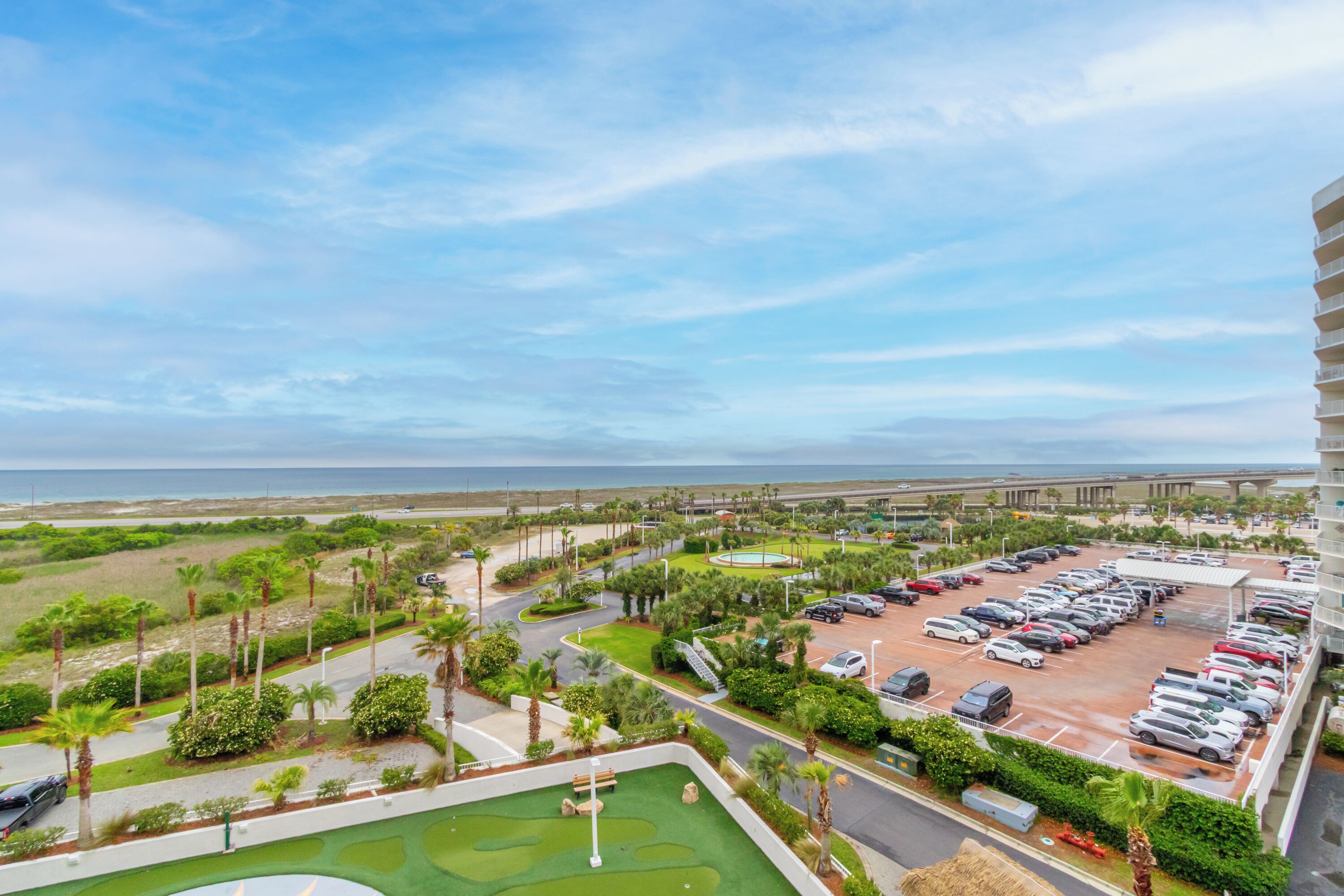 A parking lot with multiple cars, a golf course, and a view of the ocean.