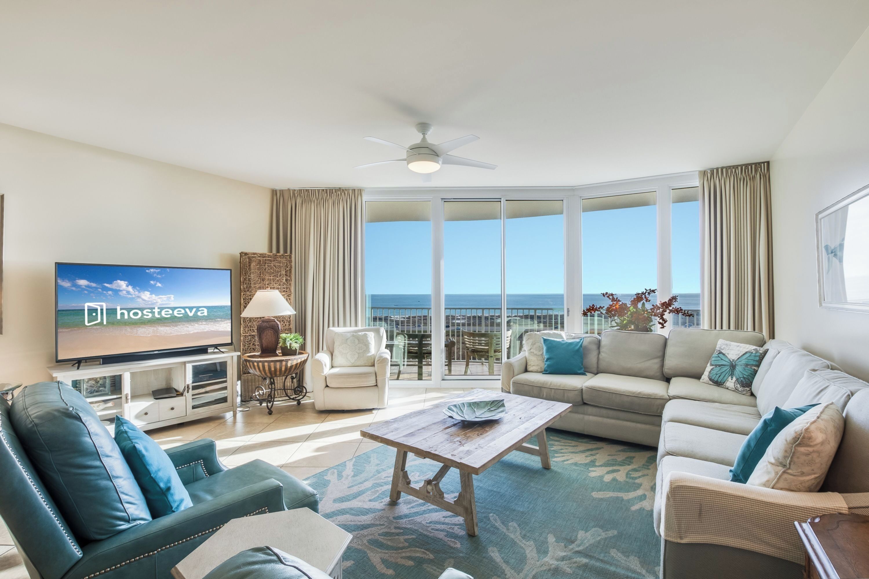 A spacious living room with a television, comfortable seating, a ceiling fan, and a view of the ocean.
