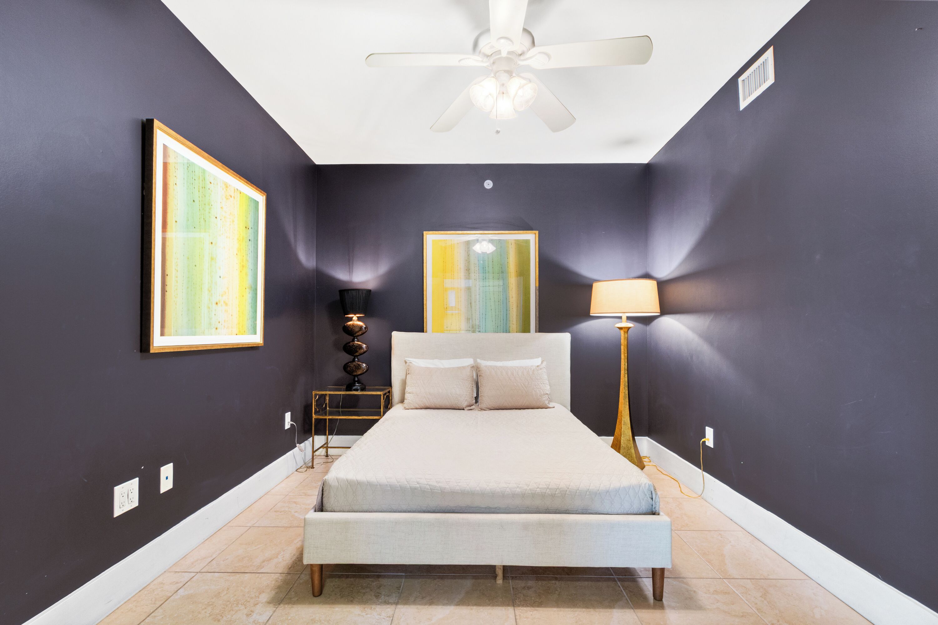 Dormitorio con cama, ventilador de techo, lámpara de pared y una obra de arte.
