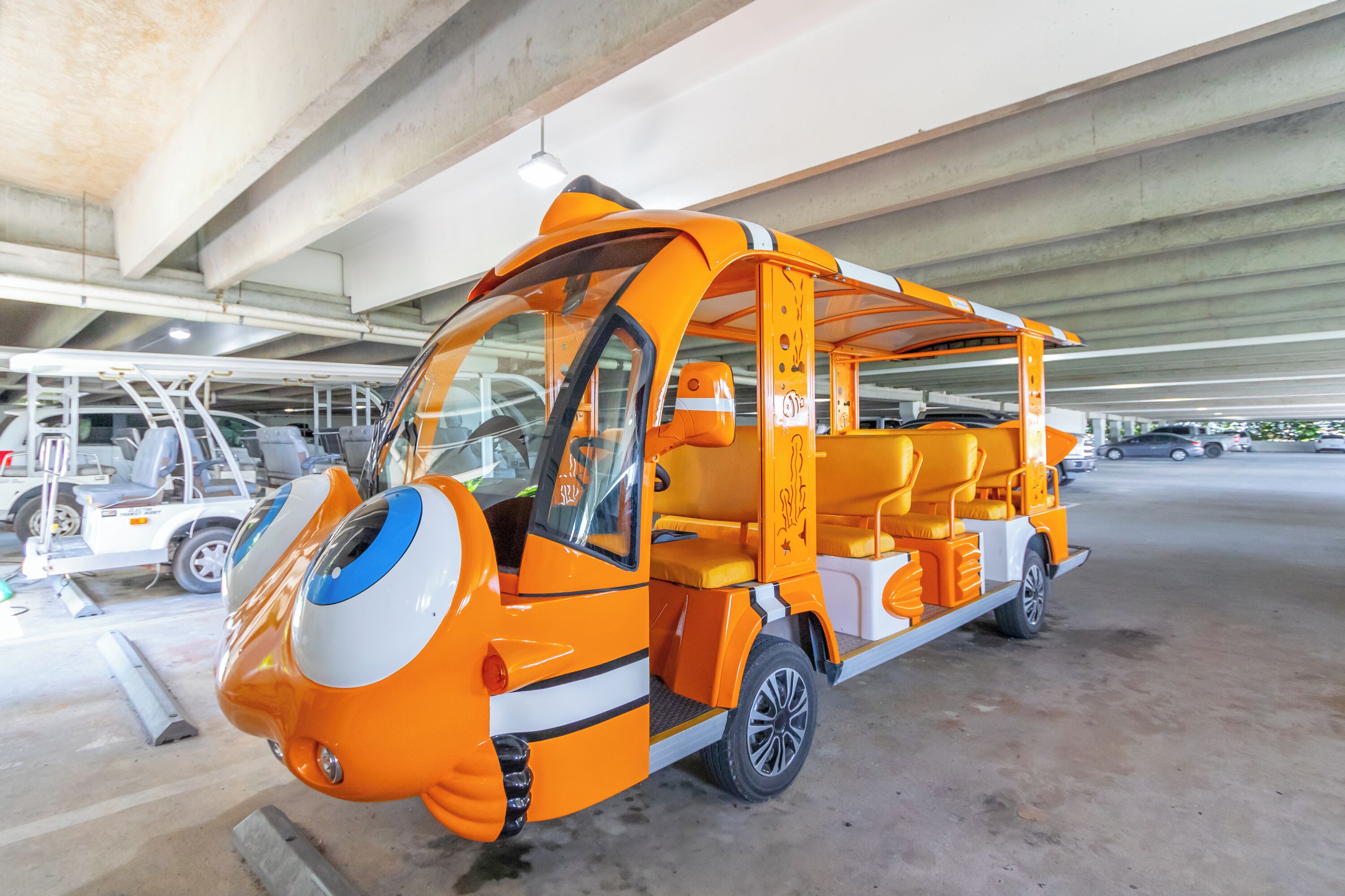 Un vehículo compacto y naranja, de diseño singular, estacionado bajo una estructura de hormigón.