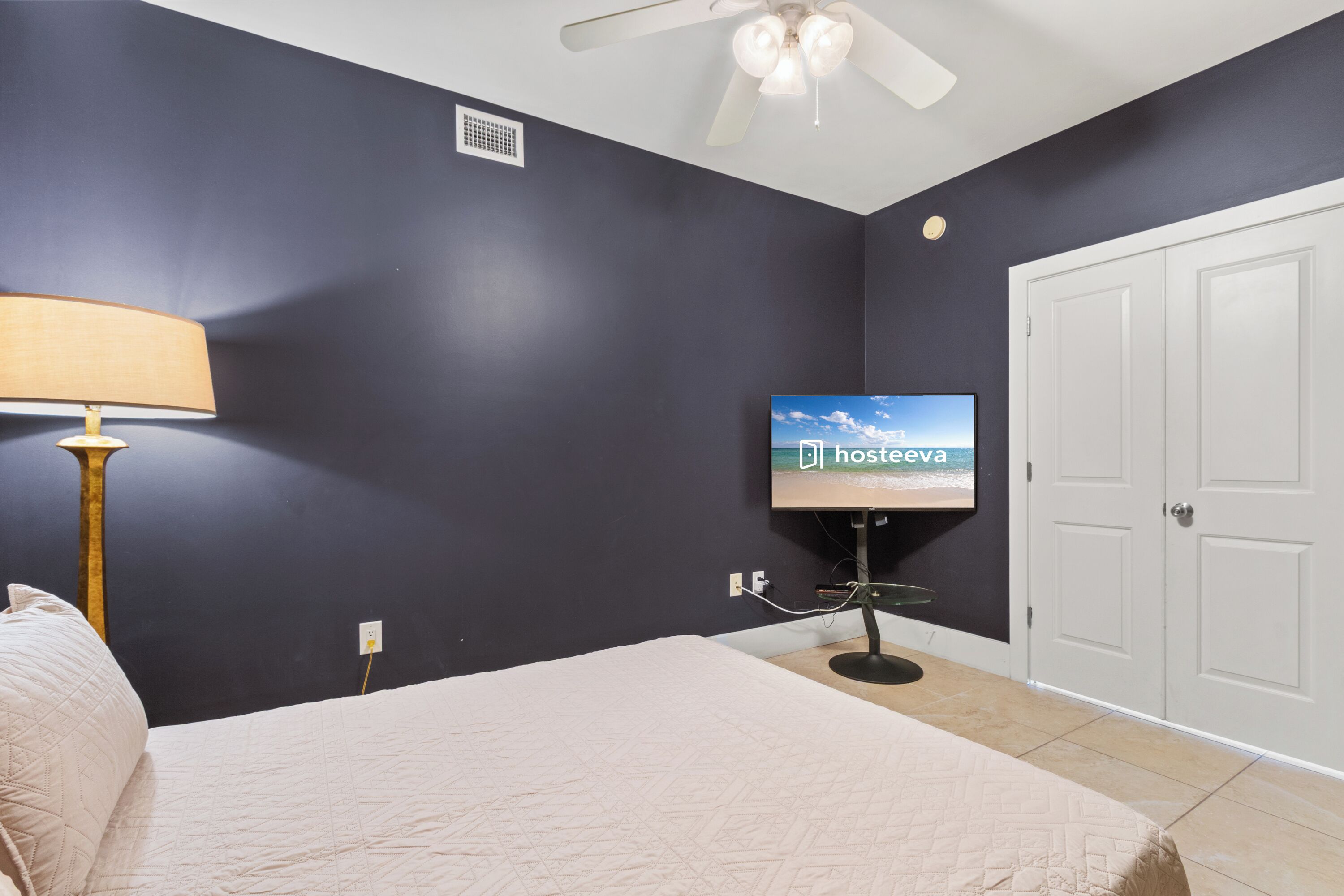 Un dormitorio con cama, ventilador de techo, televisor sobre un mueble y una puerta.