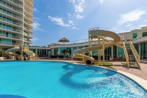 Piscina com toboáguas, edifício com varandas e céu claro.