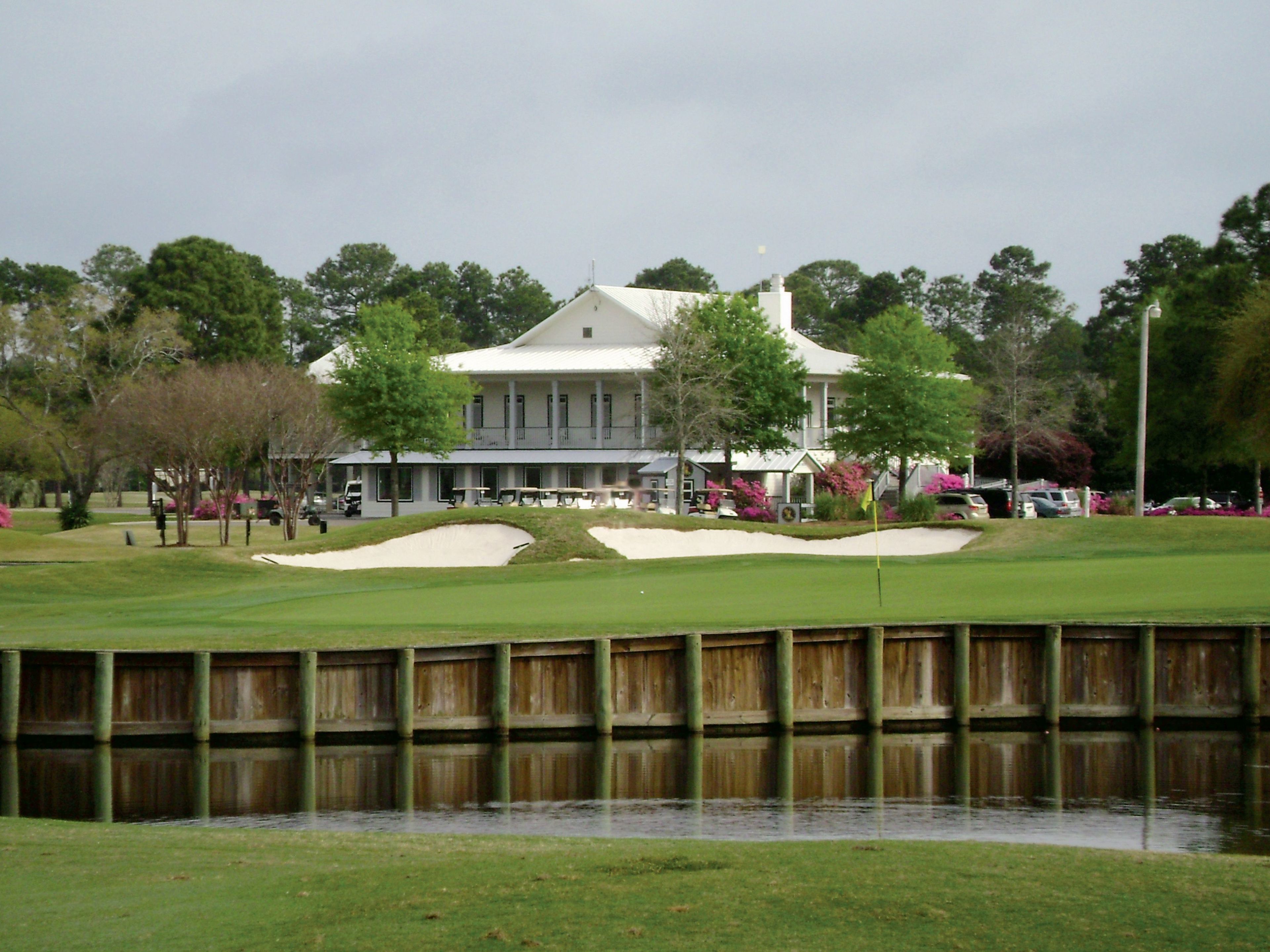 Un campo de golf con búnkeres, un obstáculo acuático y un edificio con columnas al fondo.