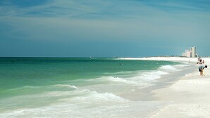 A beach with clear turquoise water, white sand, and a few people.