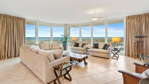 A spacious living room with large windows, a ceiling fan, and a view of the ocean.