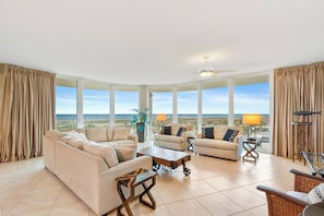 A spacious living room with large windows, a ceiling fan, and a view of the ocean.