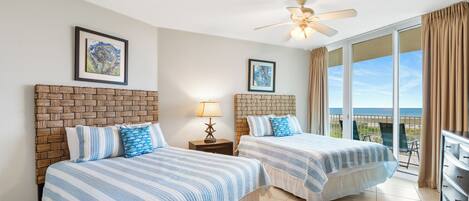 A hotel room with two beds, a ceiling fan, a large window with a view, and a brick accent wall.