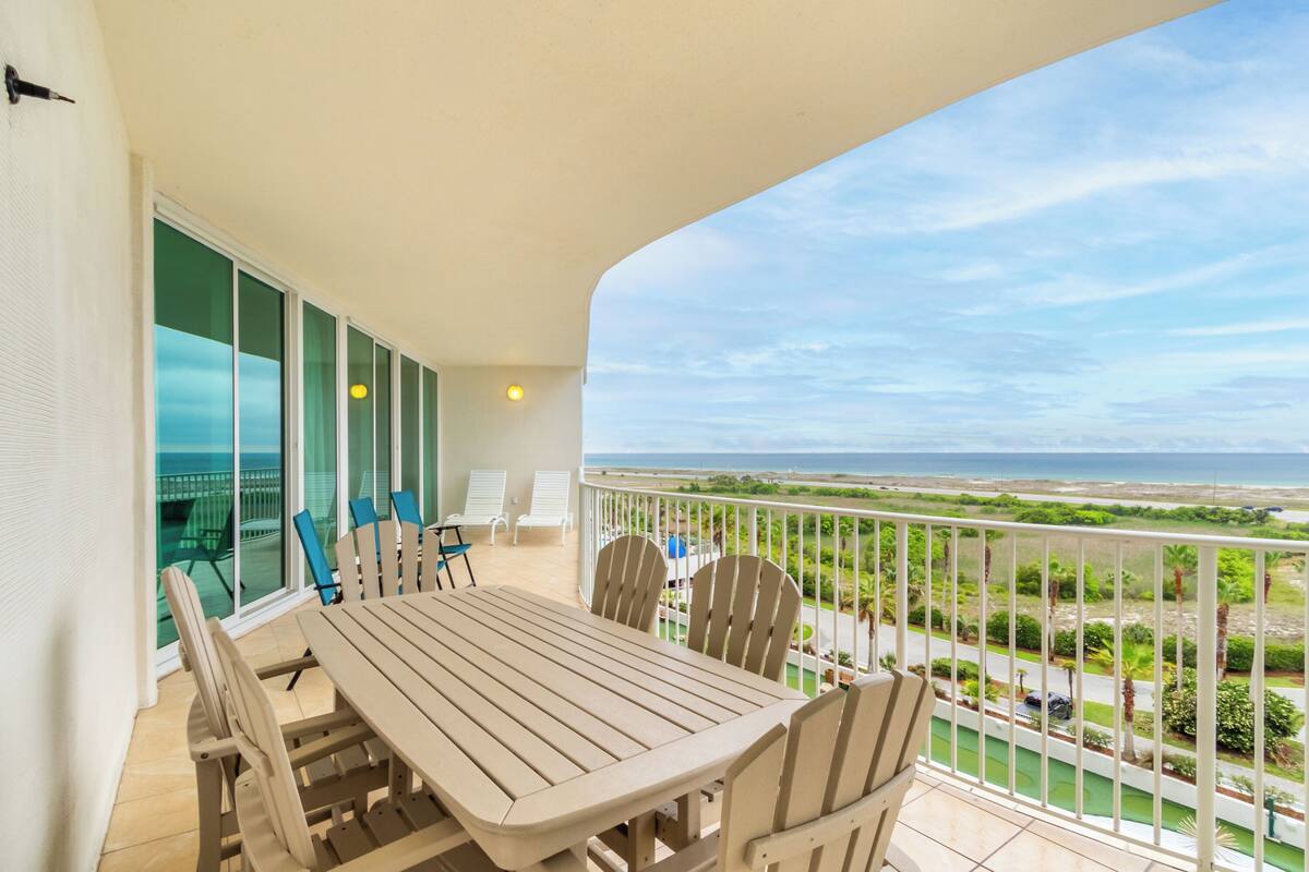 A balcony with a table and chairs, a view of the ocean, and a railing.