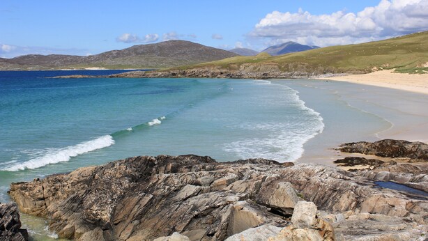 A rocky coastline with a beach and mountains in the background. - An Airigh (Stornoway)