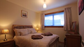 A bedroom with a bed, two bedside lamps, a window with curtains, a nightstand, and a dresser. - An Airigh (Stornoway)
