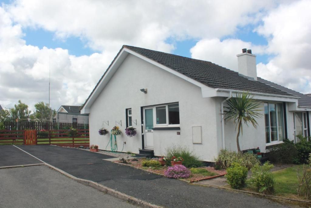 A single-story house with a white exterior, a dark roof, and a small garden with various plants and flowers.