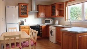 A kitchen with wooden cabinets, a built-in microwave, a washing machine, and a dining area with a table and chairs. - An Airigh (Stornoway)