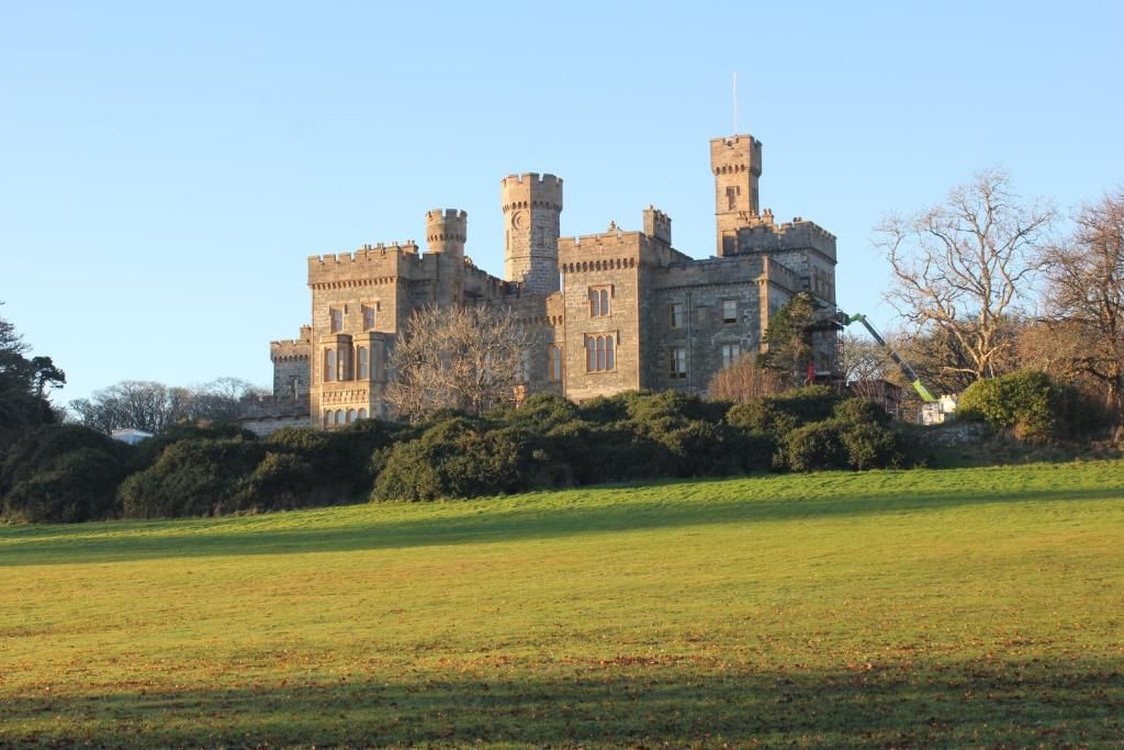 A large, historic castle with multiple towers and a well-maintained lawn in the foreground.