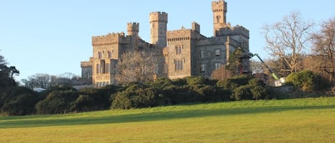 Un grand château historique, doté de nombreuses tours et d’une pelouse bien entretenue en premier plan.
