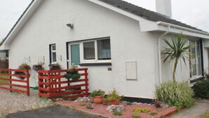 A white house with a tiled roof, a wooden fence, and potted plants in the front yard. - An Airigh (Stornoway)