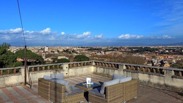 A rooftop terrace with wicker furniture and a table, overlooking a cityscape with historic buildings and a clear sky. - Domus Monamì Luxury Suites (Rome)
