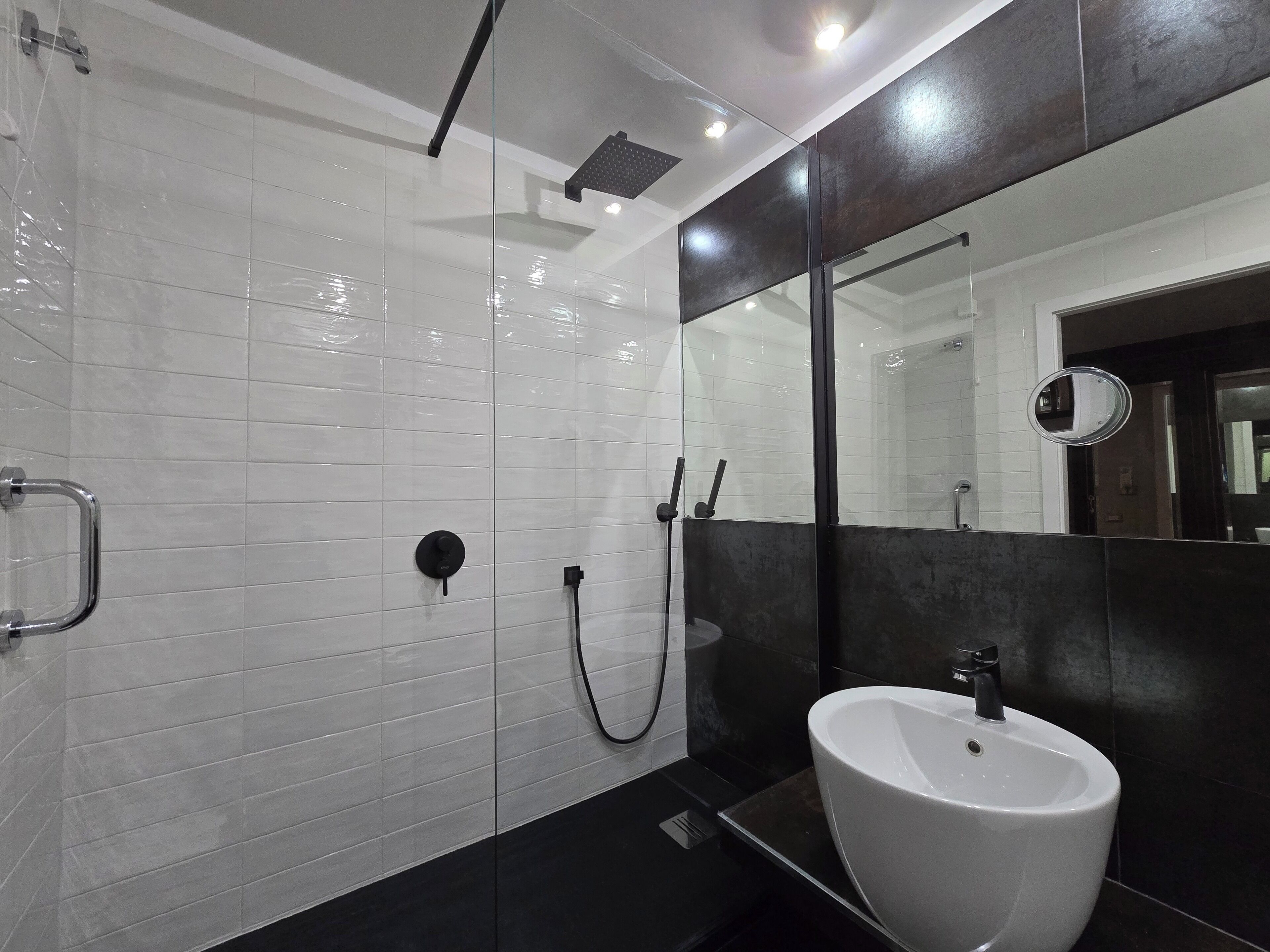 Un baño moderno con paredes de azulejos blancos, un lavamanos negro y una cabina de ducha de vidrio.