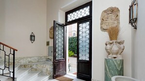 A marble staircase leading to a door with intricate glass panels, a stone lion statue, and a wall-mounted light fixture. - Domus Monamì Luxury Suites (Rome)