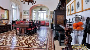 A spacious room with a patterned floor, a dining area with red chairs, a chandelier, and framed artwork on the walls. - Domus Monamì Luxury Suites (Rome)